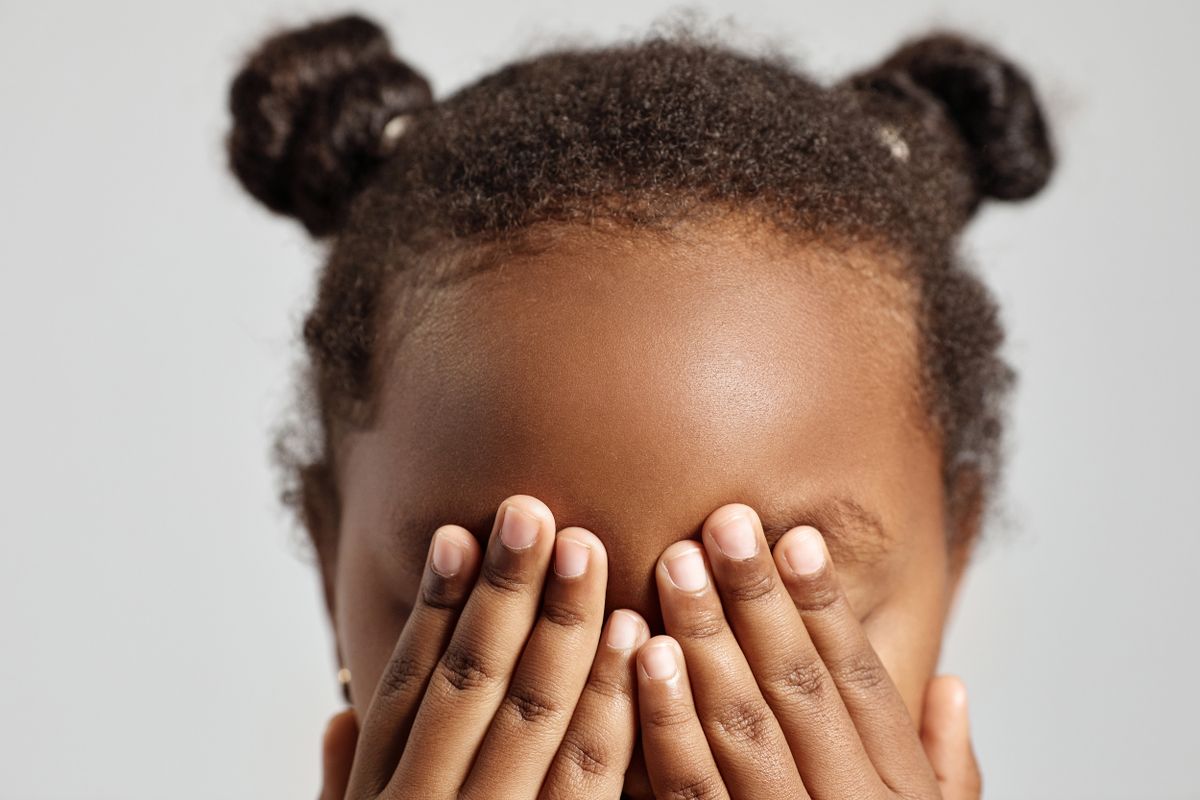 Child covering her eyes with both hands, avoiding a feared stimulus